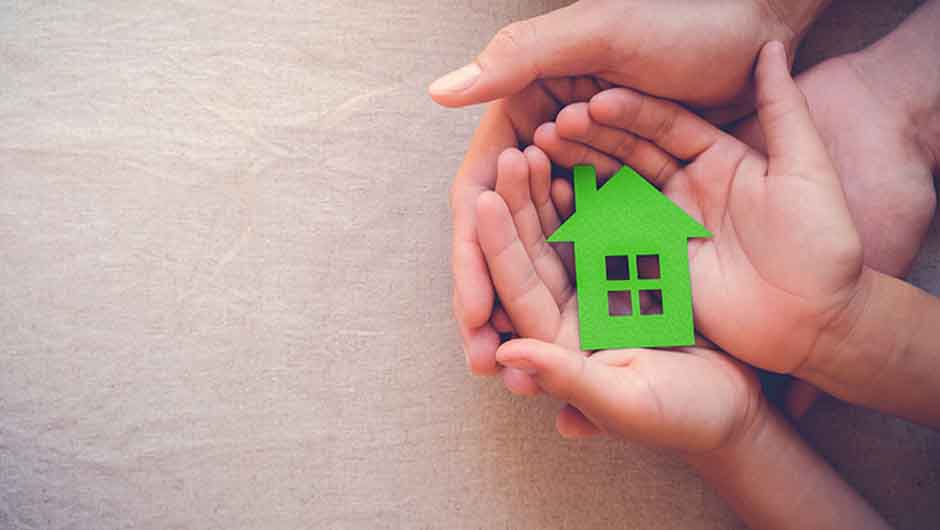 Hands holding green paper house